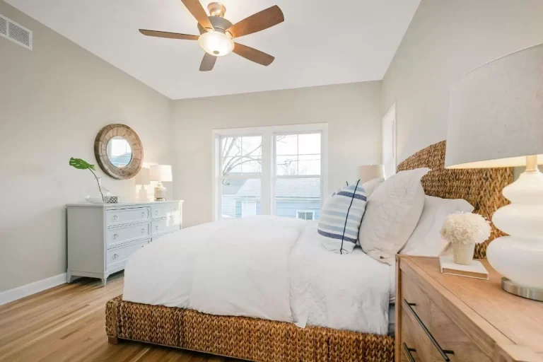 Bright, minimalist bedroom with white bedding, wooden nightstands, woven storage baskets, and ceiling fan