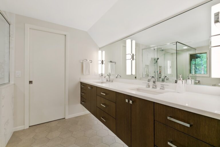 Modern bathroom with dark wood double vanity, large mirror, white subway tiles, and neutral flooring