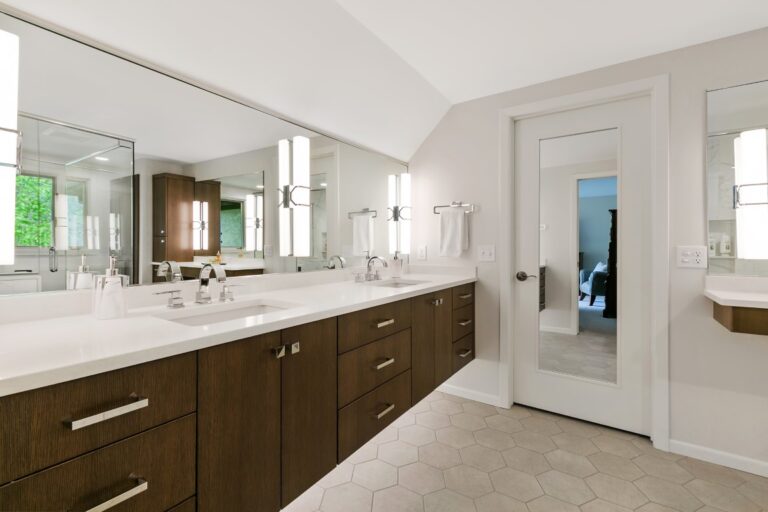 Modern bathroom with dark wood vanity, white countertop, large mirror, and double sinks