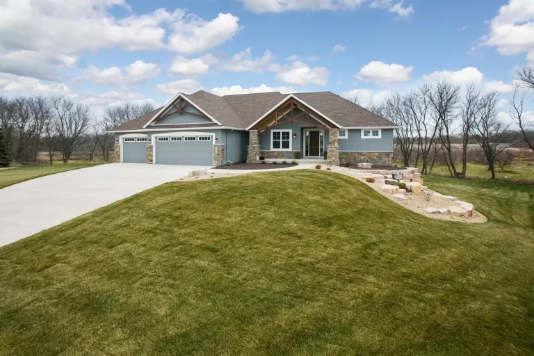 Large custom rambler home with attached two-car garage, green lawn, and bare trees in spring setting