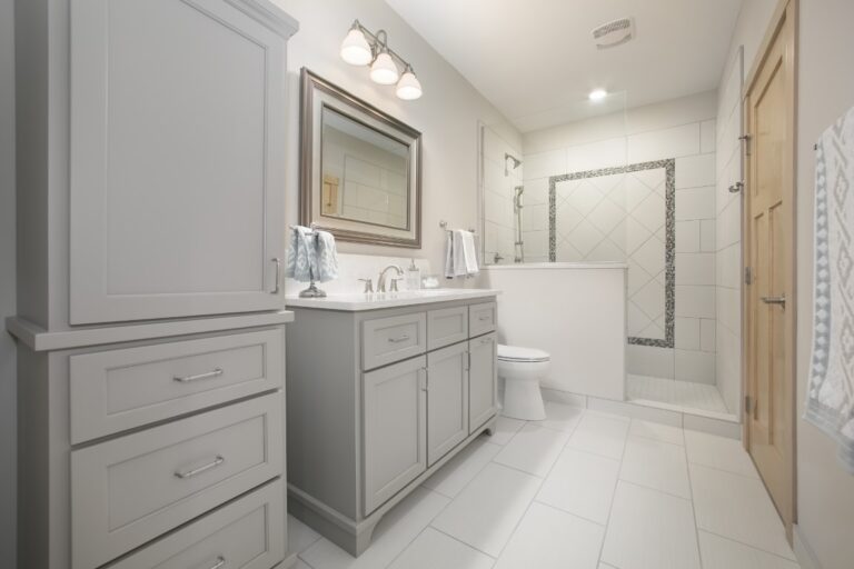Modern bathroom with gray vanity, white subway tile walls, toilet, and walk-in shower with glass enclosure