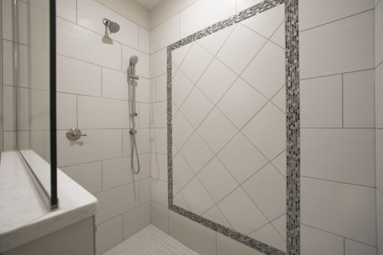 Modern bathroom shower with white subway tiles, decorative border trim, glass enclosure door, and chrome fixtures