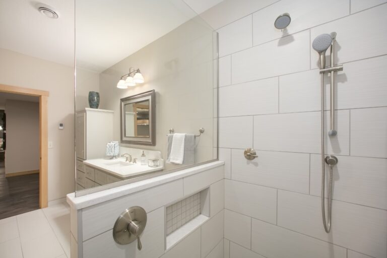 Modern white bathroom with vanity sink, large mirror, towel rack, and walk-in shower with glass enclosure