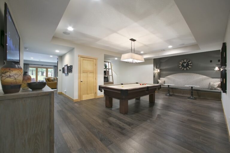 Modern basement recreation room with pool table, bar counter, kitchen area, and dark wood flooring