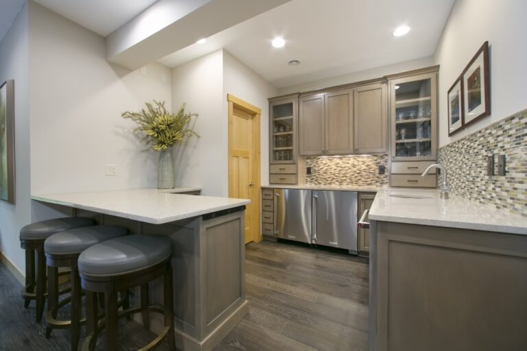 Modern kitchen with gray cabinetry, white countertops, stainless steel appliances, and a breakfast bar with seating