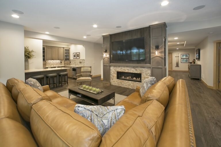 Modern living room with tan leather sectional sofa, fireplace, mounted TV, and open floor plan leading to kitchen