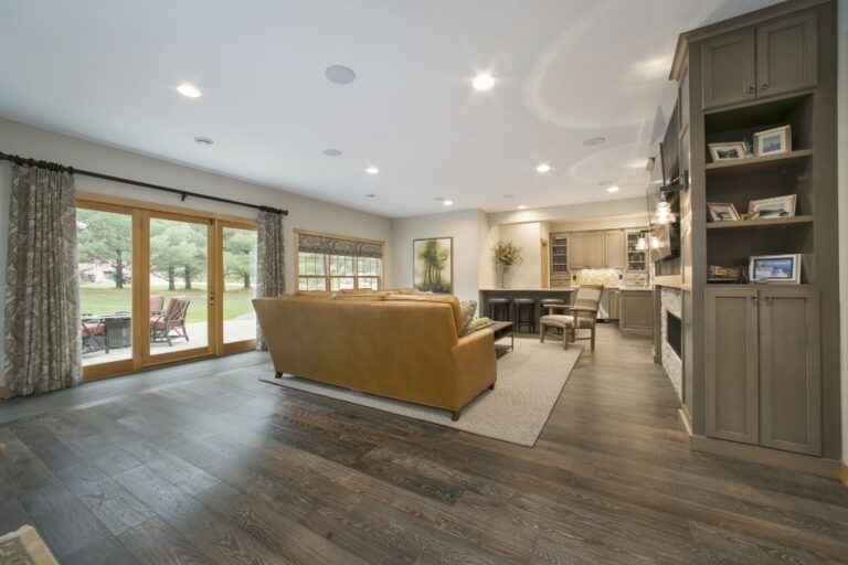Modern open-concept living room with wooden flooring, built-in shelving, glass doors, and contemporary furnishings