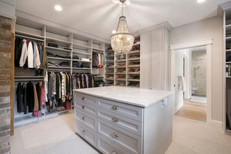 Luxury walk-in closet with white cabinetry, island dresser, built-in shelving, hanging racks, and pendant lighting