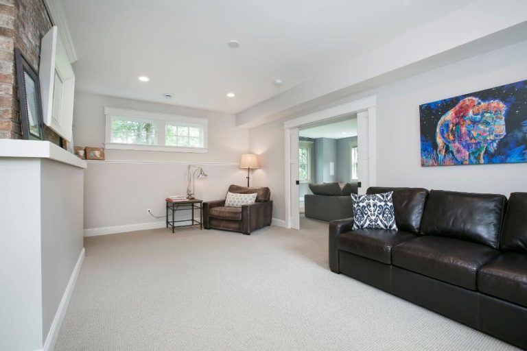 Spacious finished basement with beige carpet, black leather sofa, white walls, and colorful artwork on wall