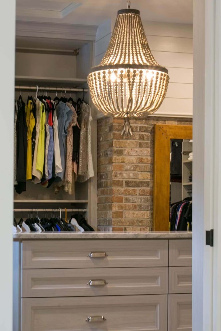 Walk-in closet with wooden beaded chandelier, gray cabinetry with drawers, brick accent wall, and hanging clothing