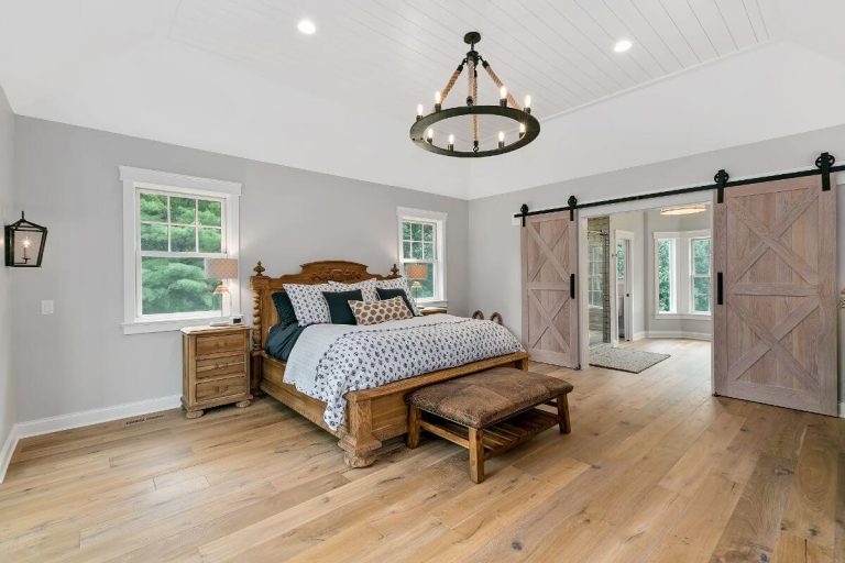 Spacious master bedroom with wooden bed, rustic decor, hardwood floors, and barn door closets