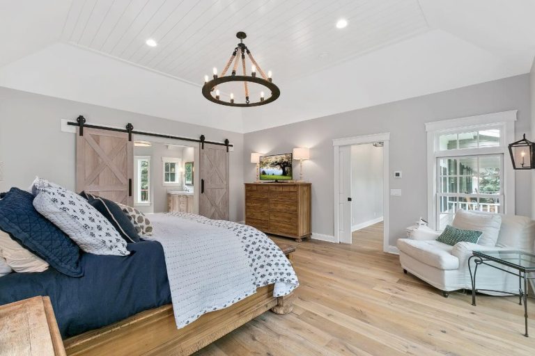 Spacious master bedroom with navy bed, hardwood floors, wooden dresser, pendant light, and glass doors leading to balcony
