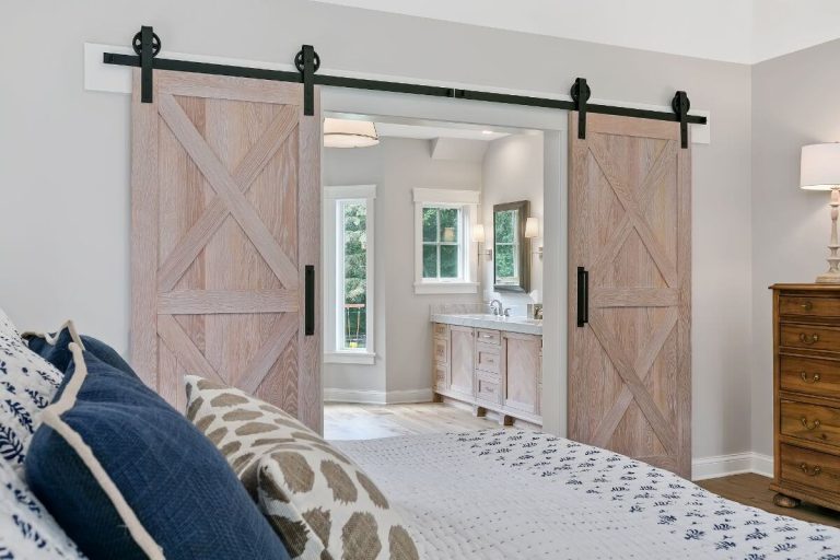 Rustic sliding barn doors with X-pattern design opening to a bright bathroom with double vanity and white subway tile