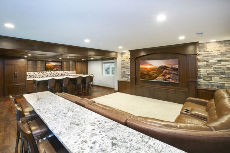 Luxury basement entertainment room with curved bar, granite countertops, stone accent wall, and flat-screen TV