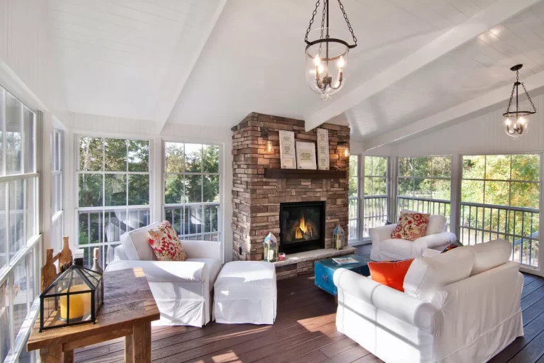 Bright sunroom with white furniture, brick fireplace, large windows, hardwood floors and pendant lighting