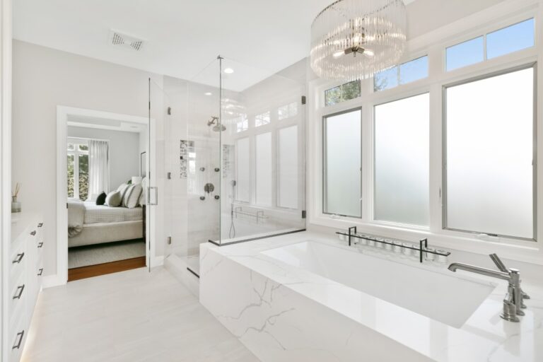 Modern white bathroom with freestanding tub, walk-in shower, large windows, and marble countertops