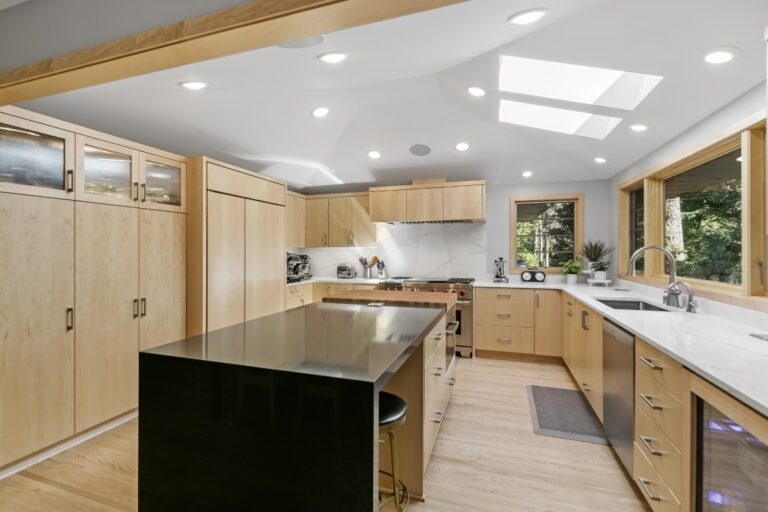 Modern kitchen with light wood cabinets, black island countertop, stainless steel appliances, and recessed ceiling lights