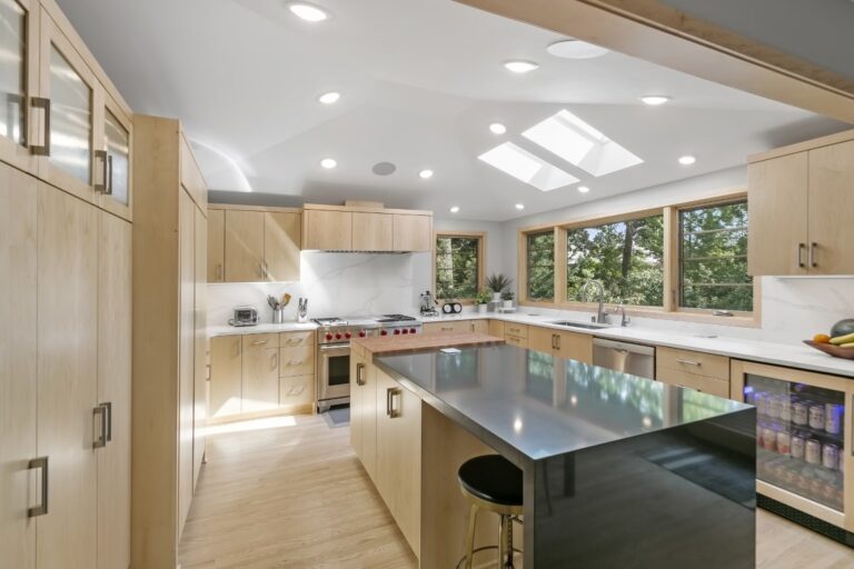 Modern kitchen with light wood cabinetry, large island with black countertop, skylight, and stainless steel appliances