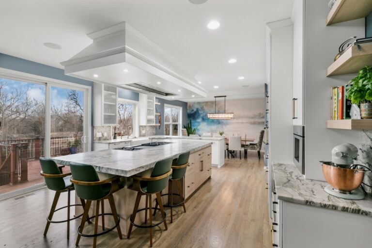 Modern kitchen with island seating, white cabinetry, stainless steel appliances, and wooden flooring overlooking a dining