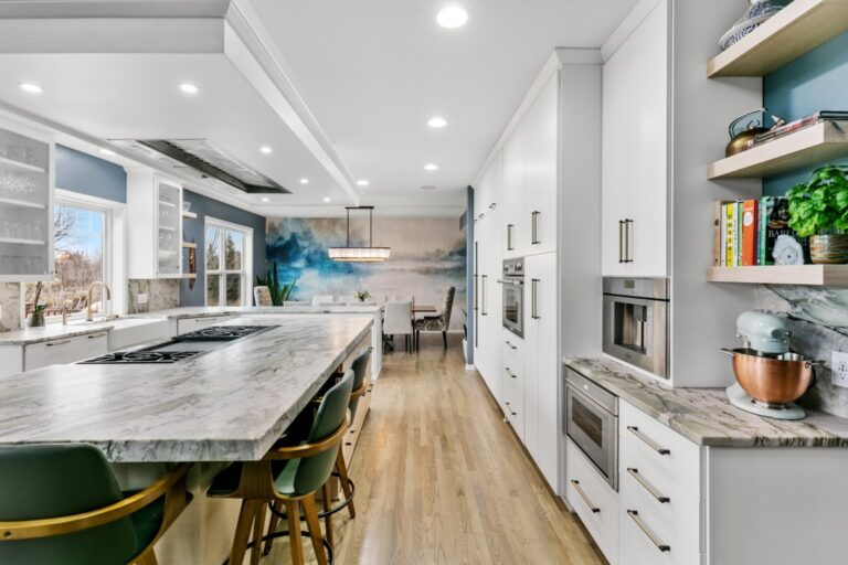 Modern kitchen with white cabinetry, marble island, green bar stools, and wood flooring