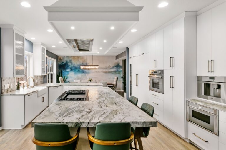 Modern white kitchen with marble island, green velvet stools, stainless steel appliances, and recessed lighting