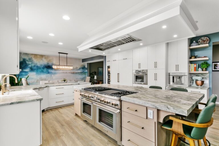 Modern white kitchen with stainless steel appliances, marble countertops, wood flooring, and open shelving