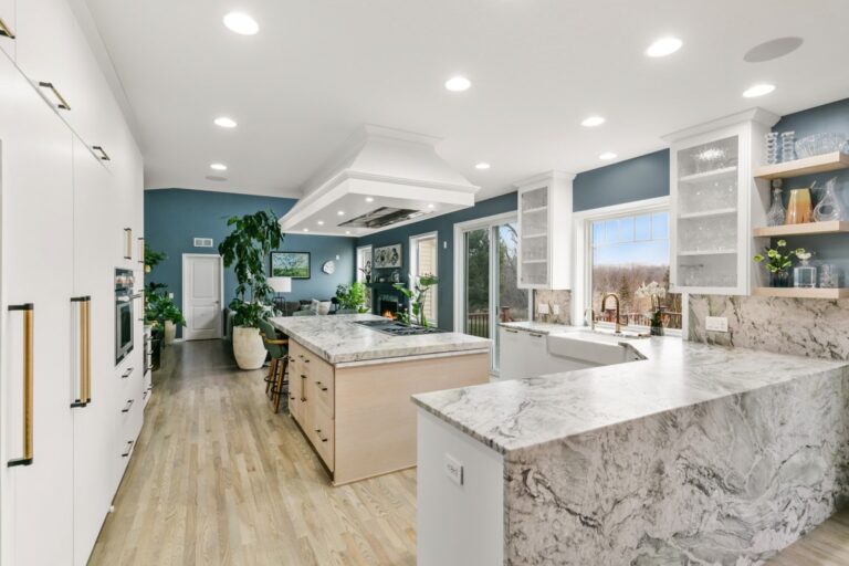 Modern kitchen with marble island, wood flooring, white cabinetry, teal accent wall, and recessed lighting