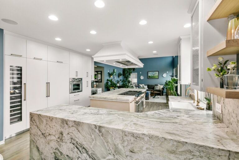 Modern kitchen with marble island, white cabinetry, stainless steel appliances, blue accent wall, and recessed lighting