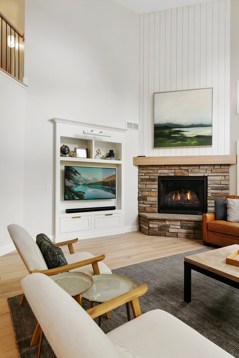 Modern living room with fireplace, wooden furniture, white walls, and landscape artwork on display