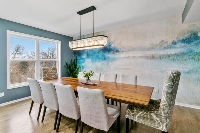 Modern dining room with wood table, upholstered chairs, teal accent wall, and blue landscape artwork