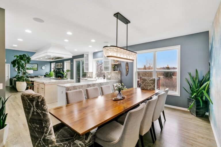 Modern open-concept dining and kitchen area with wooden table, pendant lighting, and floor-to-ceiling windows overlooking