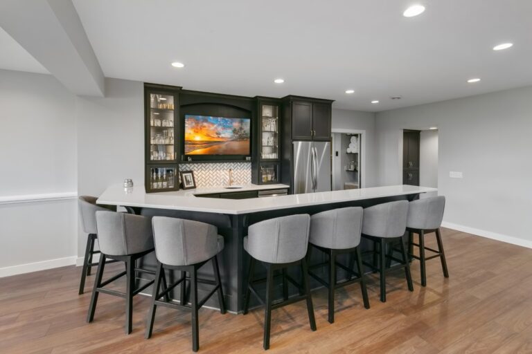 Modern kitchen with black island, six bar stools, stainless steel appliances, and dark cabinetry with artwork above