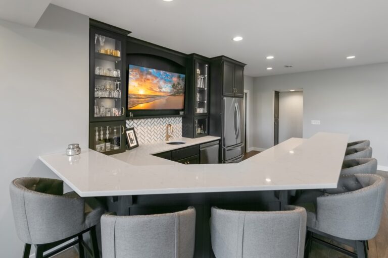 Modern kitchen with curved white countertop, gray upholstered chairs, and black cabinetry with mounted television