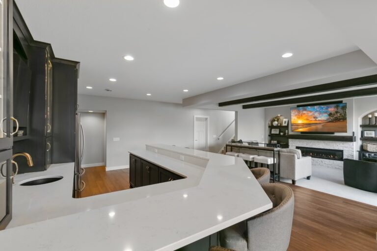 Modern kitchen with white curved island, stainless steel appliances, black cabinetry, and wood flooring