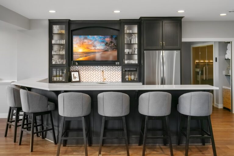 Modern kitchen with black cabinetry, stainless steel appliances, island with gray bar stools, and decorative backsplash