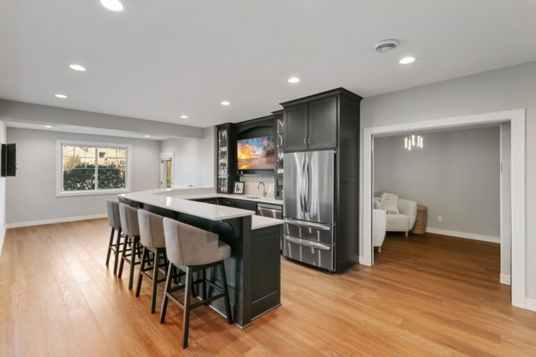 Modern kitchen with dark cabinetry, stainless steel appliances, island with seating, and hardwood flooring