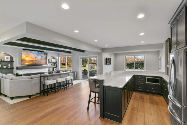 Modern open-concept kitchen and living room with white cabinetry, dark island, hardwood floors, and recessed lighting
