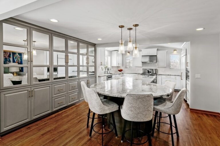Modern kitchen and dining area with round white table, upholstered chairs, wood flooring, and gray cabinetry