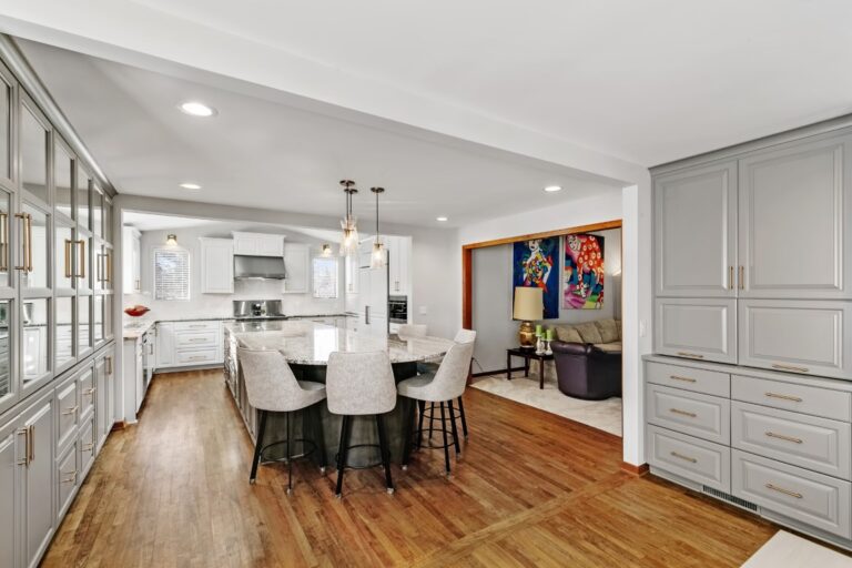 Modern kitchen and dining area with white cabinetry, island, pendant lights, hardwood floors, and artwork on wall