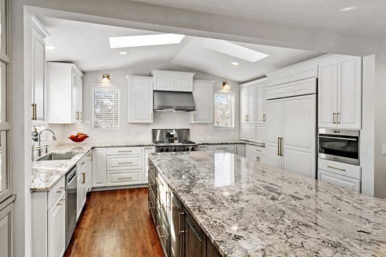 Modern white kitchen with granite countertops, stainless steel appliances, white cabinetry, and skylight windows
