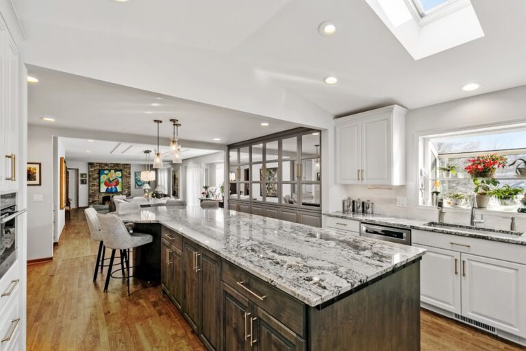 Modern kitchen with white cabinetry, marble countertops, dark island, stainless steel appliances and open floor plan