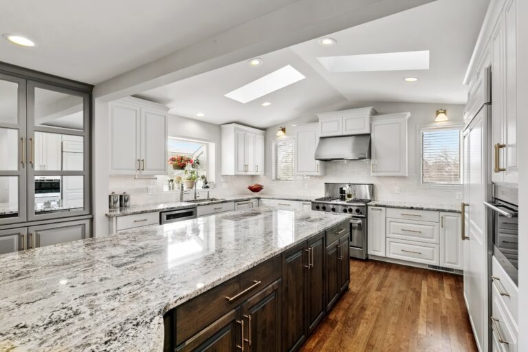 Modern kitchen with white cabinetry, granite countertops, dark island, stainless steel appliances, and skylights