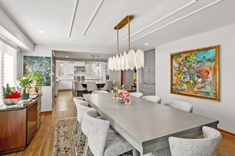 Modern open-concept kitchen and dining room with white cabinetry, gray island, pendant lighting, and contemporary artwork on