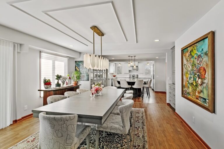 Modern kitchen with white island, wooden floors, pendant lighting, and open concept dining area with artwork