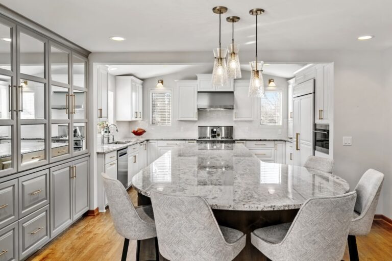 Modern kitchen with white cabinetry, marble island with bar seating, pendant lighting, and stainless steel appliances