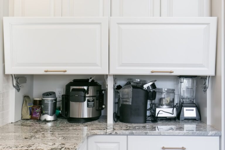 Open kitchen cabinet displaying small appliances including a pressure cooker, coffee maker, and other countertop devices on