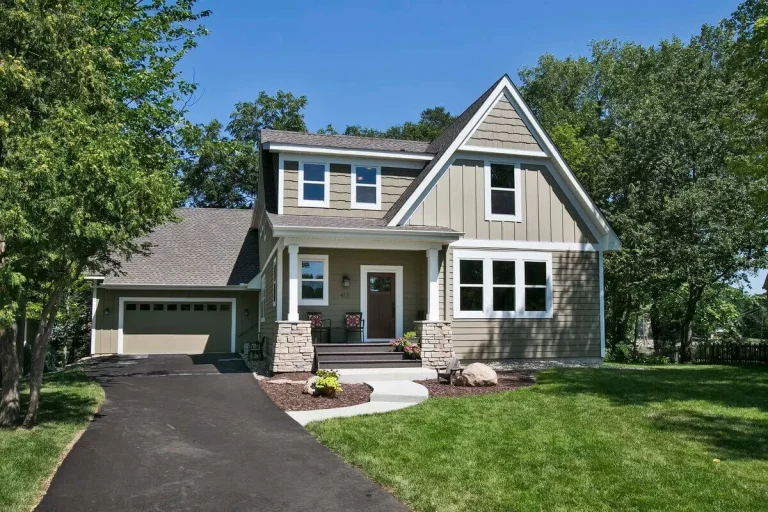 Two-story blue and white house with attached garage, white trim, front porch, and landscaped yard with green trees